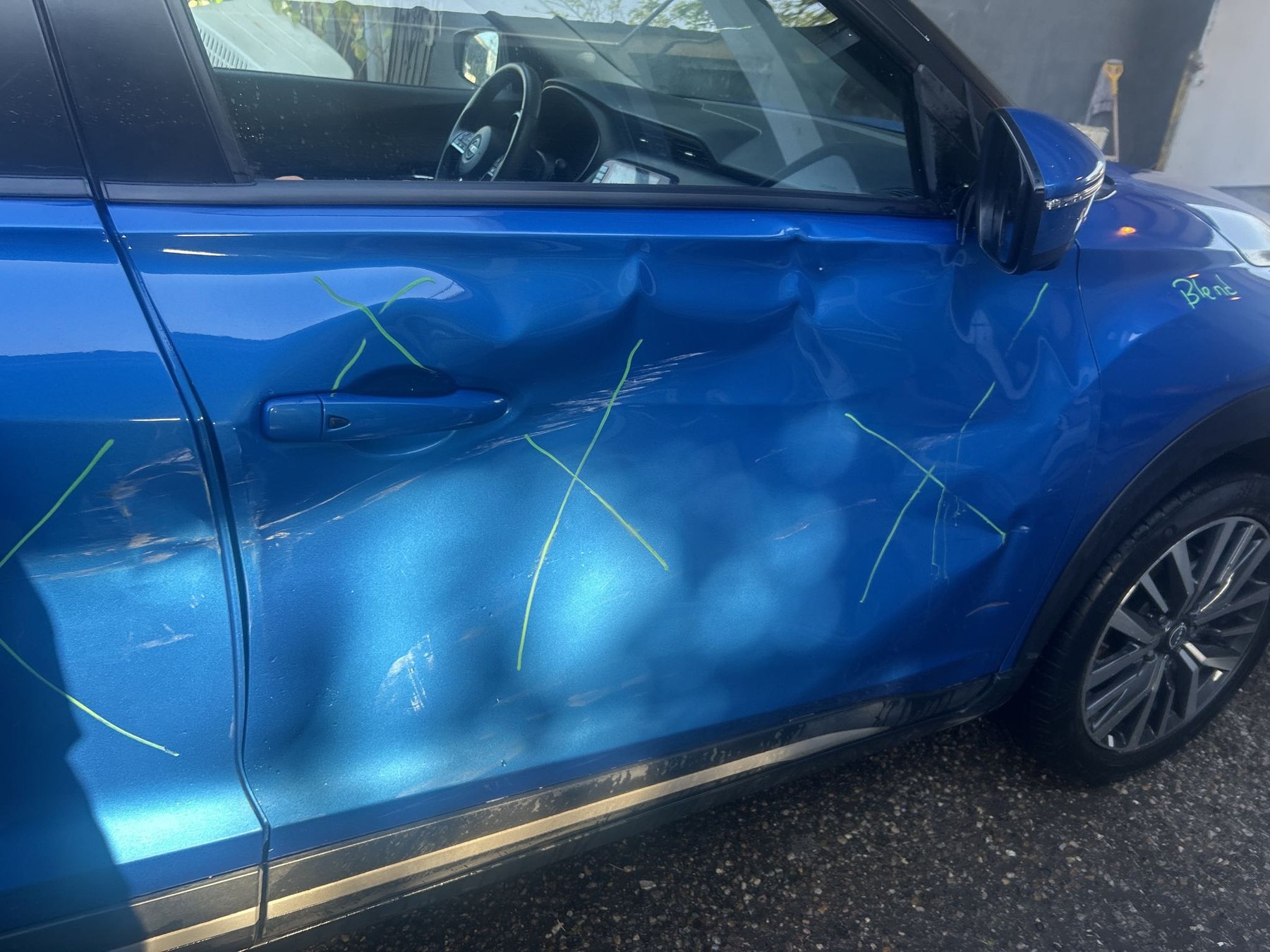 Blue crossover with extensive driver-side door and fender damage before repair